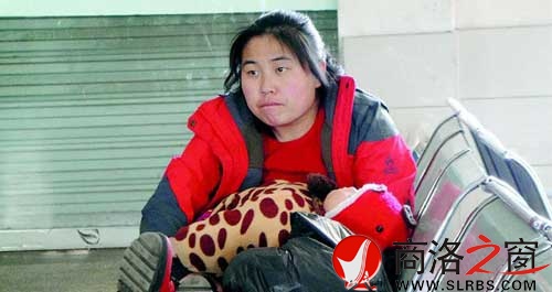 候車廳里，一位母親抱著睡著的孩子發(fā)呆
